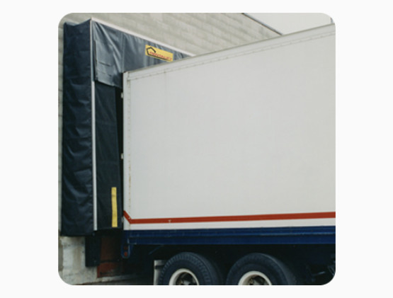 A truck backed up to a loading dock with black loading dock seals Windsor surrounding the entrance, and part of a gray building wall visible in the background.